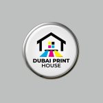 C ircular button featuring the logo of "Dubai Print House" with a stylized house icon and CMYK color stripes (cyan, magenta, yellow, and black) symbolizing printing beneath the house. The text "DUBAI PRINT HOUSE" is written below the graphic.